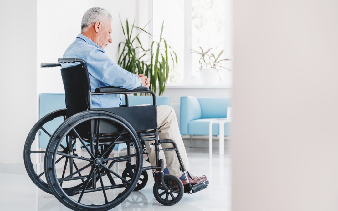 Sad elderly man sitting in wheelchair while looking out in window in retirement house
